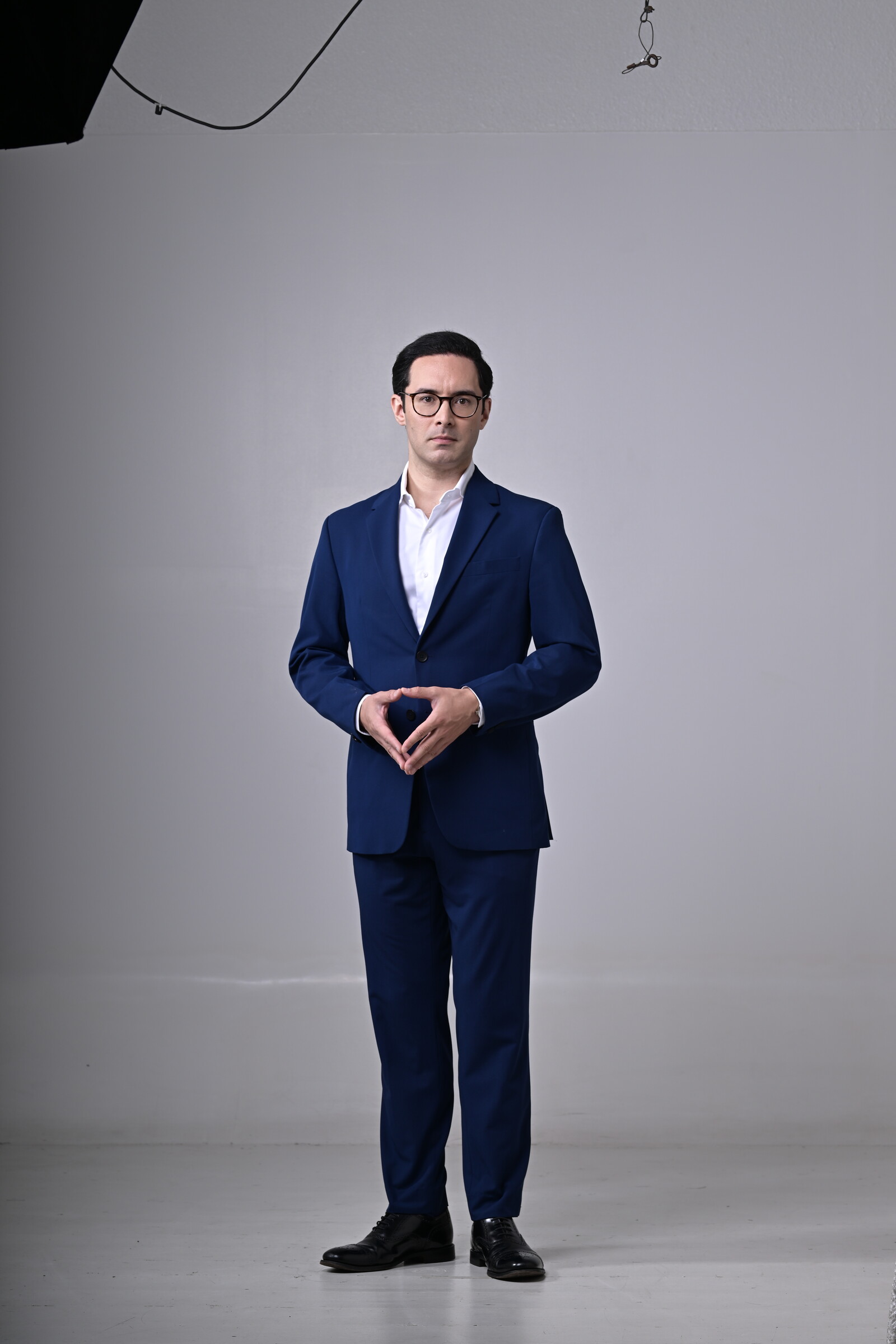 Dr Mark McKelvie in a navy suit, standing against a quiet grey studio background.
