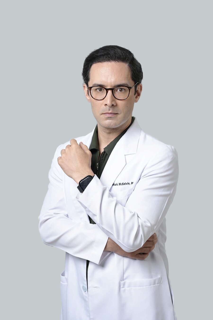 Dr Mark McKelvie in a white clinical coat, arms folded, studio portrait.