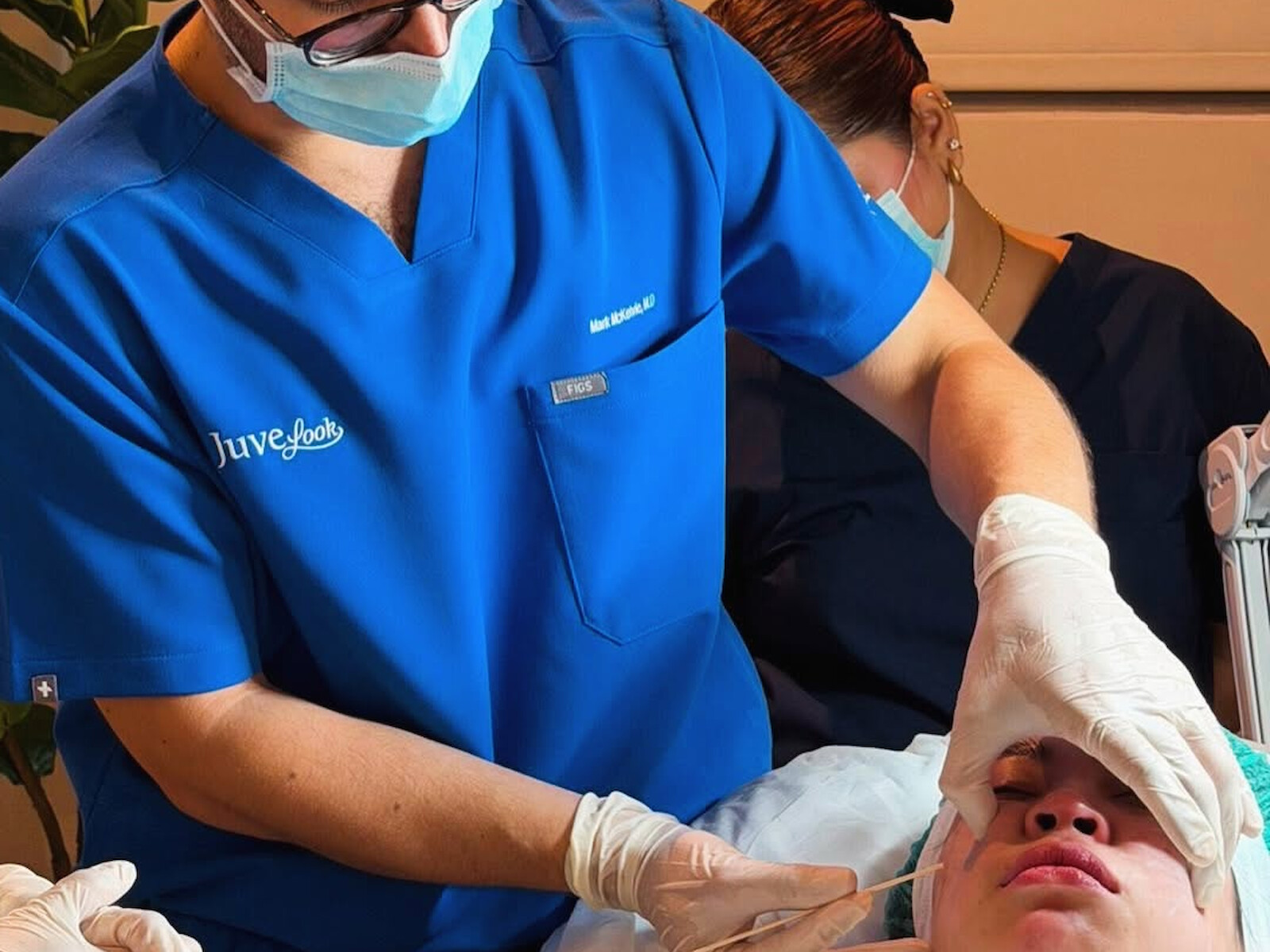 Dr McKelvie working with a fine instrument at a patient&rsquo;s cheek, both hands gloved.