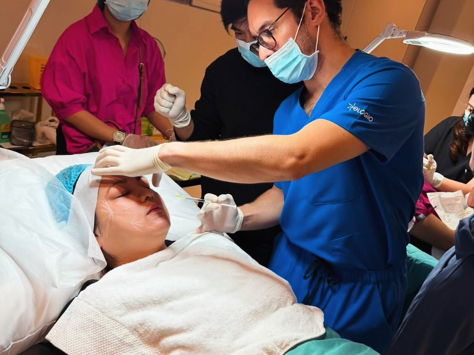 Dr McKelvie assessing a patient&rsquo;s skin under a procedure lamp, an assistant alongside.